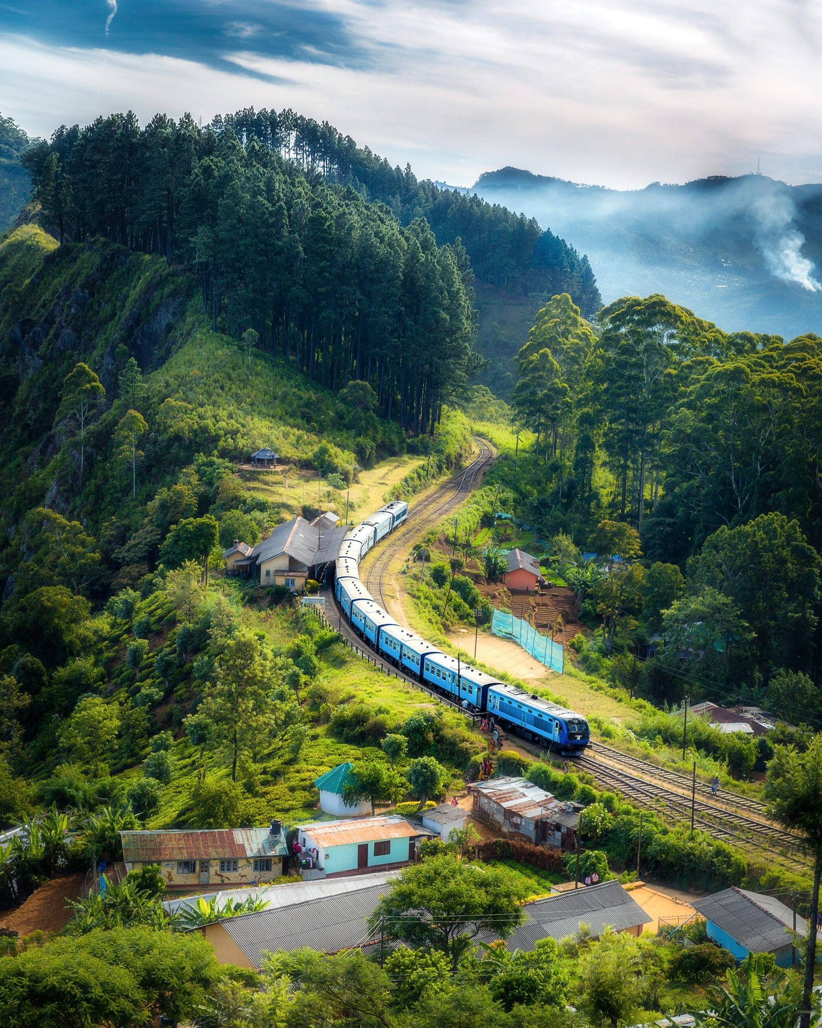 Aerial view of a picturesque train winding through lush green hills and rural houses.